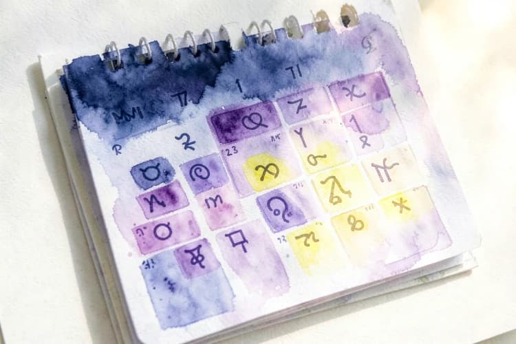 Um close-up de um calendário com os meses do ano destacados, com símbolos do zodíaco sobrepostos.